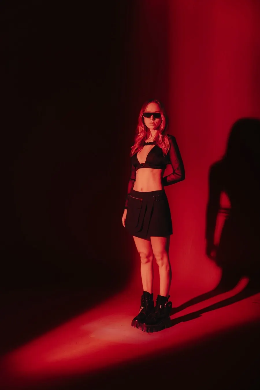 Luana Digier contra una pared iluminada de rojo, con anteojos oscuros